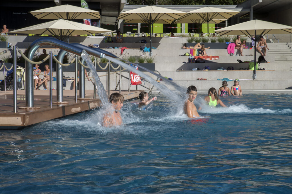 Kinder im Wasser - Im Hintergrund Personen die sich sonnen